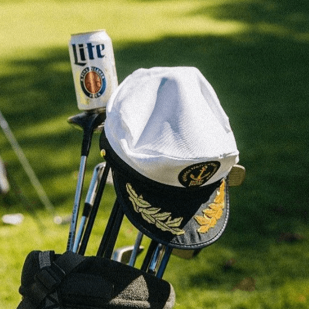 A party captain hat and a beer on a caddy bag of golf clubs